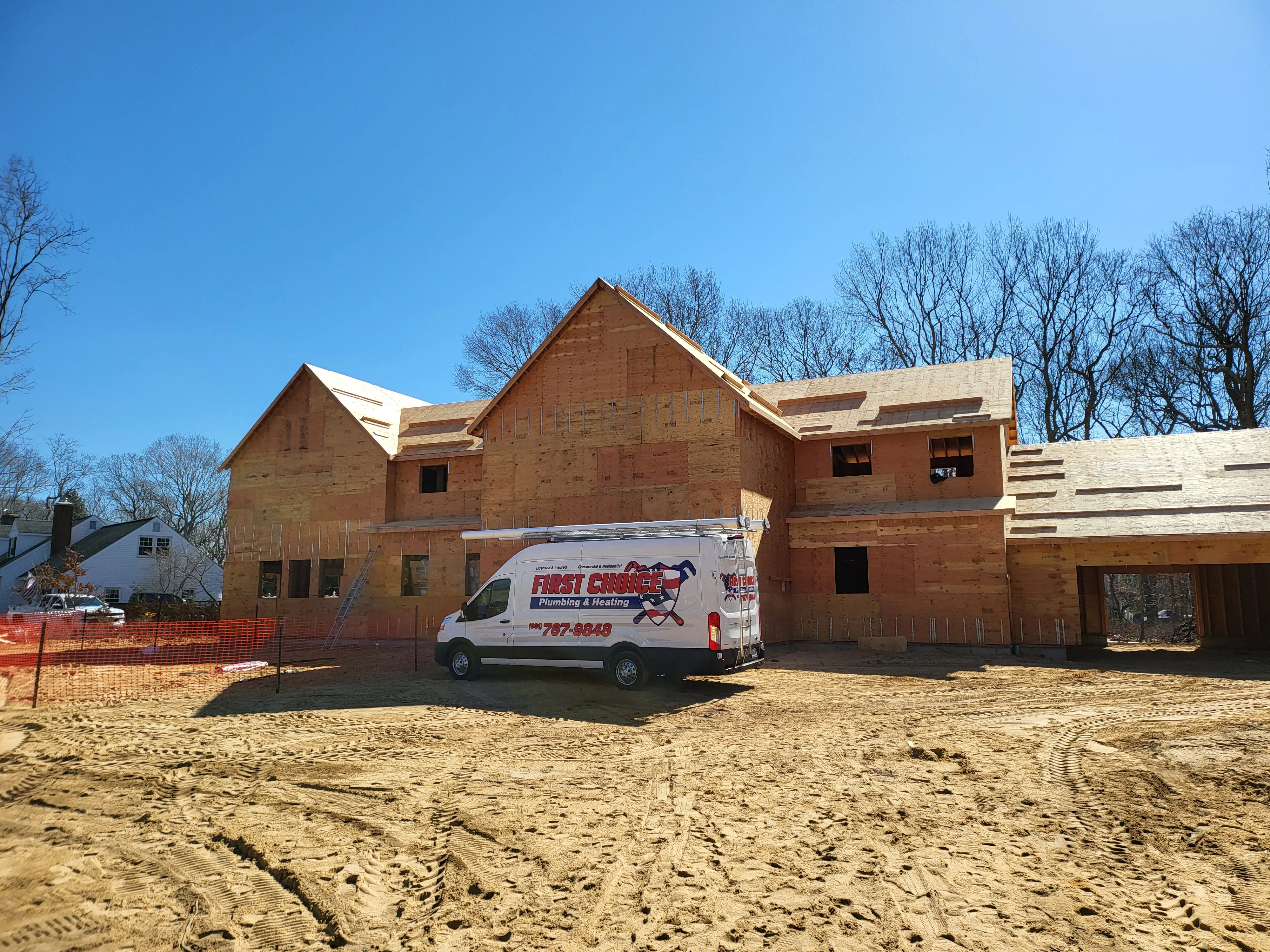 Brick home under construction with plumbing service van parked in front, rough framing visible