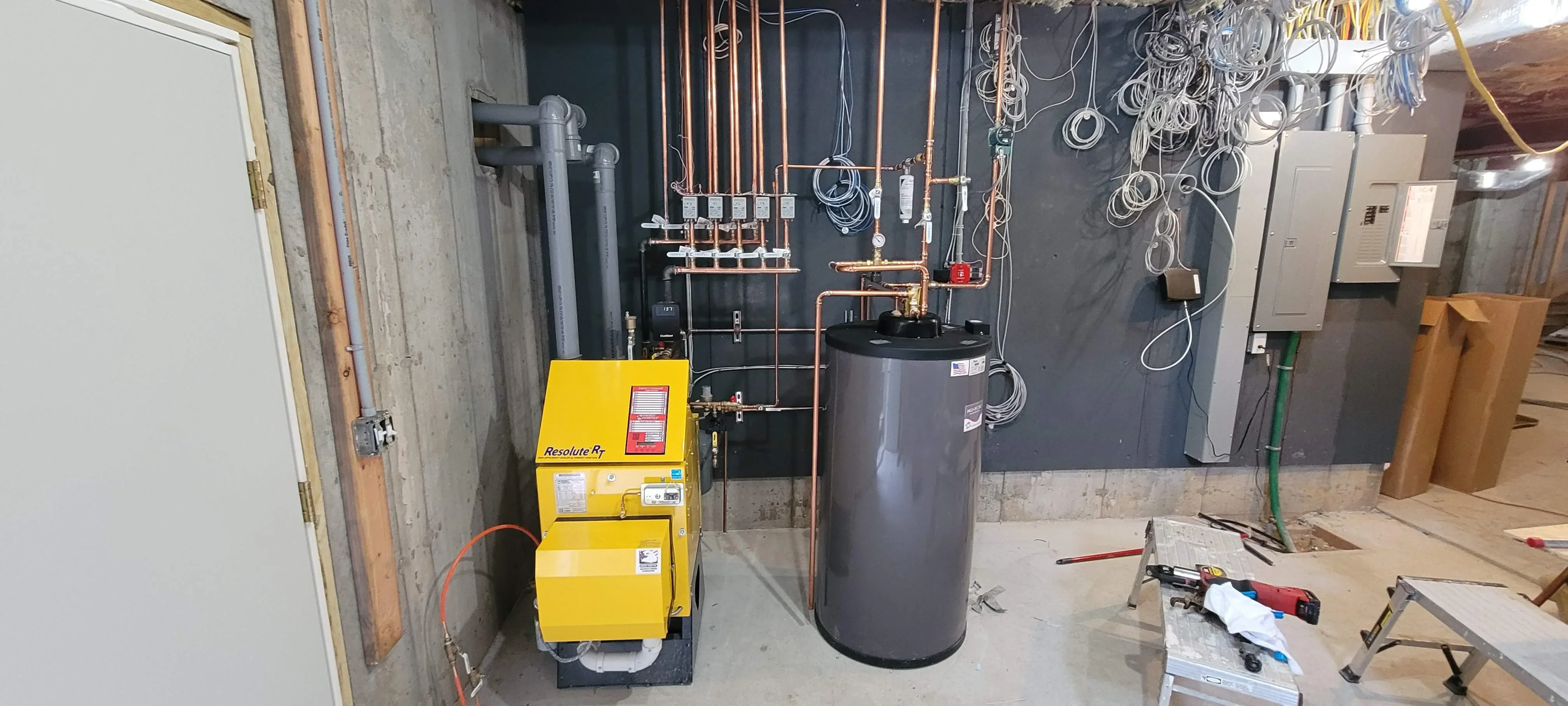 Yellow condensing boiler, gray storage tank, copper piping, and radiant heating manifold installation